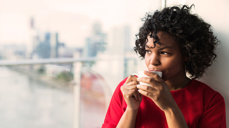 Close-up of a woman standing by the window drinking coffee.