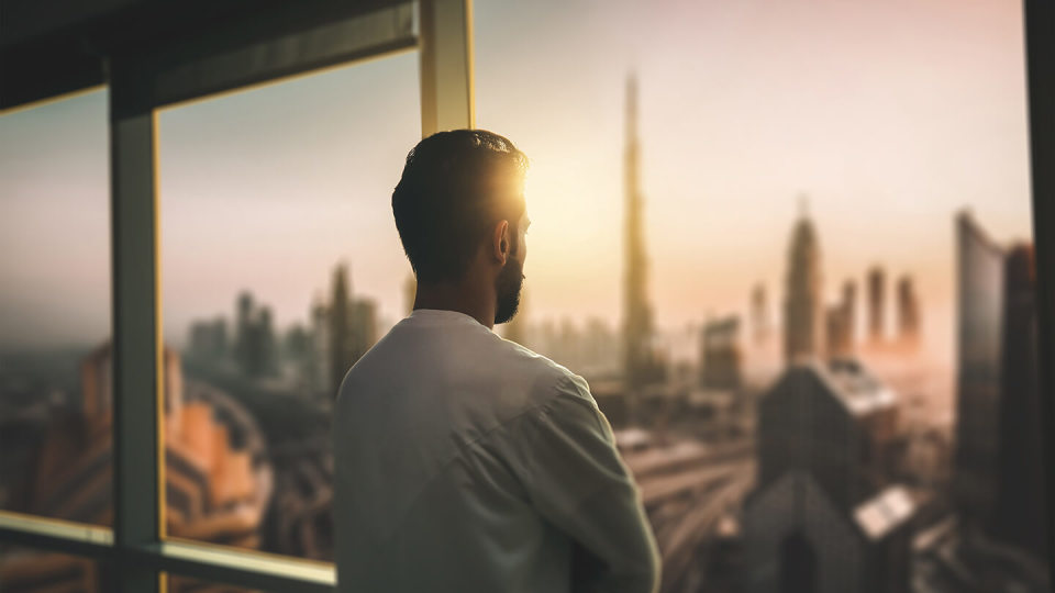 Arabic business man looking out through the office balcony seen through glass window. arab young man looking at Dubai city through hotel window.